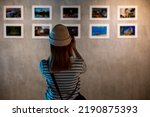 Photographer visit at photo frame to leaning against at show exhibit artwork gallery, Asian woman takes picture art gallery collection in front framed paintings pictures on white wall with camera