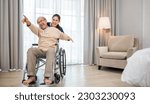 Small photo of Asian senior retired old man sitting on wheelchair having fun with young woman nurse, Happy curator person doctor pushing and running elderly patient freedom raising arm, sanatorium