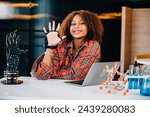Small photo of Black teenage student in a classroom learns and tests a robotic arm on a table delving into subjects of interest. Embracing innovation and technology for skill development in education.