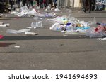 street pollution - trash and plastics flying on the city pavement with anonymous pedestrians walking through garbage in dirty, polluted streets