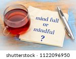 Mind full or mindful   Inspiraitonal handwriting on a napkin with a cup of tea.