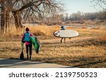 Small photo of Evans, CO, USA - March 26, 2022: Female paddlers are carrying their inflatable stand up paddleboards to launch for early spring paddling trip on the South Platte River in Colorado