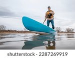 solo senior male paddling a stand up paddleboard on a lake in early spring, frog perspective from an action camera at water level