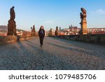 Happy young woman with long hair is walking through the Charles bridge. View at distance of St. Vitus Cathedral and historical center of Prague Castle, buildings and landmarks of old town. Czech Repub