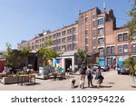 Small photo of PECKHAM, UK - MAY 19, 2018: People drinking and hanging around outside a bar in the trendy Copeland Park in South London. The Bussey Building is in the background.