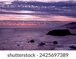 Small photo of California's beautiful Goat Rock Beach during the golden hour of sunset with yellow skies peeking through picturesque clouds and ocean waters lapping against rocks jettison from the ocean's waters.