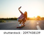 Beautiful young girl sits on longboard in sunny weather.