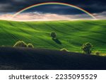 Scenic view of rainbow over green field. dramatic gray sky over a picturesque hilly field

