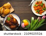 Small photo of Easter food on dark rustic table: pastel colored eggs, roasted chicken and vegetables, buns and spring flowers tulips top view flay lay, Easter family dinner meal with festive dishes, space for text
