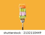 Close-up of fork with food on it: delicious fillet salmon, cucumber, onion, green salad on orange background. Concept of healthy diet and clean eating with fish and vegetables, balanced nutrition