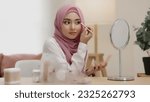 Small photo of Daily routine make up young Asian beautiful muslim woman with hijab looking mirror applying eyes shadow daily routine at home. Beautiful of girl holding brush make-up on eyes.