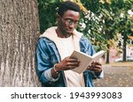 Portrait of young african man student reading a book wearing an eyeglasses in autumn city park