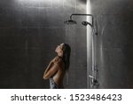 Young woman standing under shower and washing hair back to the camera over black ceramic tiles in modern luxury dark bathroom interior.