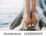 Boho styled girl wearing indian silver jewelry on the beach, tanned legs close up