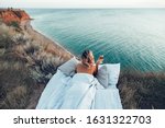 Woman drinking wine enjoying view on beach landscape while relaxing in bed on mountain in sunset on the edge of Earth. Calm and quiet wanderlust concept moment when person feels happiness and freedom.