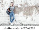 Hipster girl wearing blank gray t-shirt, jeans and backpack posing against rough street wall, minimalist urban clothing style, mockup for tshirt print store
