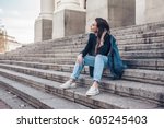 Fashion model wearing ripped boyfriend jeans, jacket and sneakers posing in the city street. Fashion urban outfit. Casual everyday clothing style.