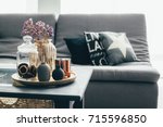 Home interior decor in gray and brown colors: glass jar with dried flowers, vase and candle on the wooden tray on the coffee table over sofa with cushions. Living room decoration.