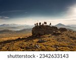 Big diverse group of hikers silhouettes stands at mountain top and looks at sunset
