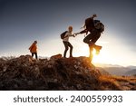 Group of young hikers with backpacks walks with backpacks and helps each other in climbing in sunset mountains