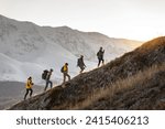 Small photo of Group of young active hikers with backpacks walks uphill in mountains at sunset