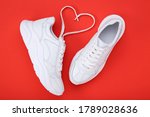 Pair of white shoes and shoelaces in shape of heart on red background
