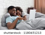 Happy african-american couple in bed with laptop browsing in internet, copy space