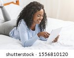 African pretty girl reading blog on digital tablet lying in bed, free space