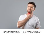 Small photo of Middle aged sick man having sore throat, looking at copy space over grey studio background. Bearded man touching his red neck, suffering from throat disorder, tonsillitis, throat cancer, cold