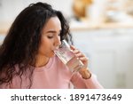 Healthy Liquid. Beautiful Brunette Woman Drinking Mineral Water From Glass In Kitchen, Thirsty Young Lady Enjoying Refreshing Drink At Home, Closeup Portrait With Selective Focus, Free Space