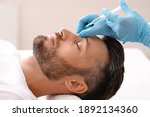 Side view of middle-aged man getting beauty injection in nose at aesthetic clinic. Plastic surgeon injecting anti-aging filler in handsome bearded man nose, having plastic correction, closeup
