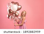 Small photo of Party time. Charming blonde woman in stylish dress holding bunch of birthday balloons over pink studio background, copy space. Joyful young lady having fun celebration, enjoying holiday