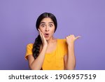 Small photo of Wow, Look Here. Amazed young indian woman pointing at copy space over purple studio background. Excited surprised lady indicating free space, showing place for advert or promotional text