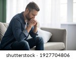 Sad bearded middle-aged man in casual sitting on couch at home, leaning on hands and looking down, upset man having problems, side view, copy space. Loneliness, depression, financial hangover concept