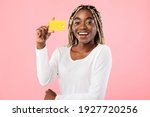 Easy Payment Concept. Portrait of smiling casual young African American woman holding debit credit card in hand and showing it to camera, standing and posing isolated over pink studio background