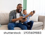 Small photo of Joyful African Father And Kid Boy Playing Videogames At Home