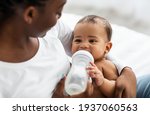 Small photo of African American woman feeding her child from baby bottle