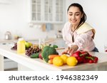 Healthy Food To Boost Your Immune System. Beautiful smiling young woman cooking fresh organic salad at home in modern kitchen, reaching for vegetables, copy space. Diet, Food And Lifestyle Concept