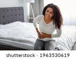 Small photo of People, Healthcare and Health Problem Concept. Portrait of upset sick young black woman suffering from acute pain in right side, sitting on bed at home, free copy space. Abdomen liver pain