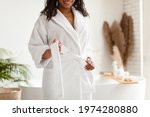Unrecognizable African American Lady Untying White Bathrobe Preparing For Beauty Ritual Standing In Modern Bathroom In Hotel Spa Center. Female Beauty And Body Care. Cropped