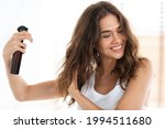Hairspray Advertisement. Happy Woman Applying Spray On Wavy Hair For Detangling Caring For Herself Standing In Modern Bathroom Indoors. Hairstyling Product For Split Ends