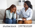Upset black lady with nervous breakdown consulting psychologist, having session with counselor at clinic. Professional psychotherapist comforting depressed female patient at office