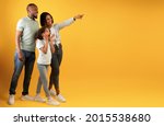 Small photo of Wow offer. Full body length portrait of excited black family looking and pointing aside at copy space on yellow background, demonstrating free place for your advert, panorama, banner