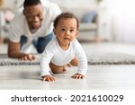 Happy Black Father Looking At Adorable Infant Baby Crawling On Floor At Home, Proud African American Dad Spending Time With His Cute Toddler Child, Enjoying Paternity Leave, Selective Focus