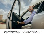 Small photo of Positive young middle-eastern man going out the car, low angle photo, copy space. Happy arab guy open automobile door and smiling, getting in. Auto test-drive, leasing, buying, renting concept