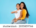 Small photo of Arabic Girl And Her Mom Showing Vaccinated Arm And Thumbs Up Gesture After Covid-19 Vaccination Sitting Over Blue Background, Studio Shot. Coronavirus Protection For Kids Concept