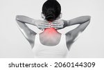Small photo of Rear back view of tired young woman touching inflammated zone on her neck, suffering from cervical osteochondrosis, massaging and rubbing lightened with red area, blue and white grey studio background