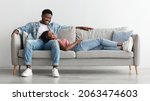 Small photo of Free Time Together. Happy beautiful African American couple spending weekend resting on couch indoors at home in living room, relaxing and enjoying the company of each other, woman lying on man's lap