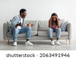 Small photo of Breaking Up And Divorce Concept. Young married black couple having fight, guy yelling at crying lady, gesturing at home. Furious man shouting at his wife or girlfriend, sitting on sofa at living room