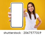 App Ad. Smiling pretty woman holding smartphone with white blank device screen in hand close up to camera, orange studio. Gadget with empty free space for mockup, banner isolated, selective focus